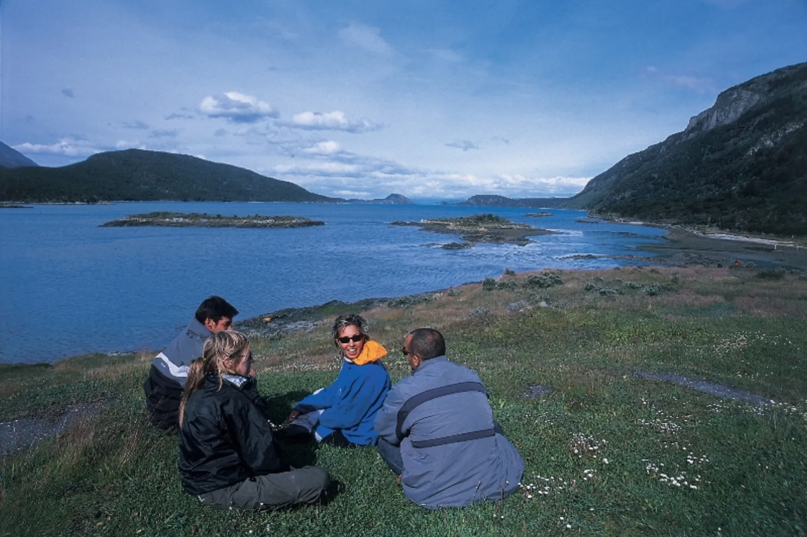 Visitors resting on the grass above a bay in Tierra del Fuego National Park