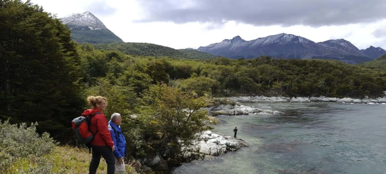 Hikers above a river with snowy mountains behind