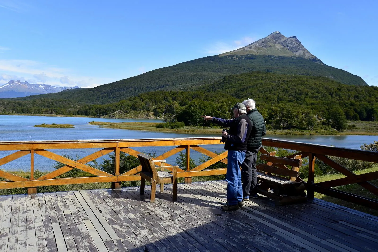 Couple on a wooden viewing deck above a lake and a green peak