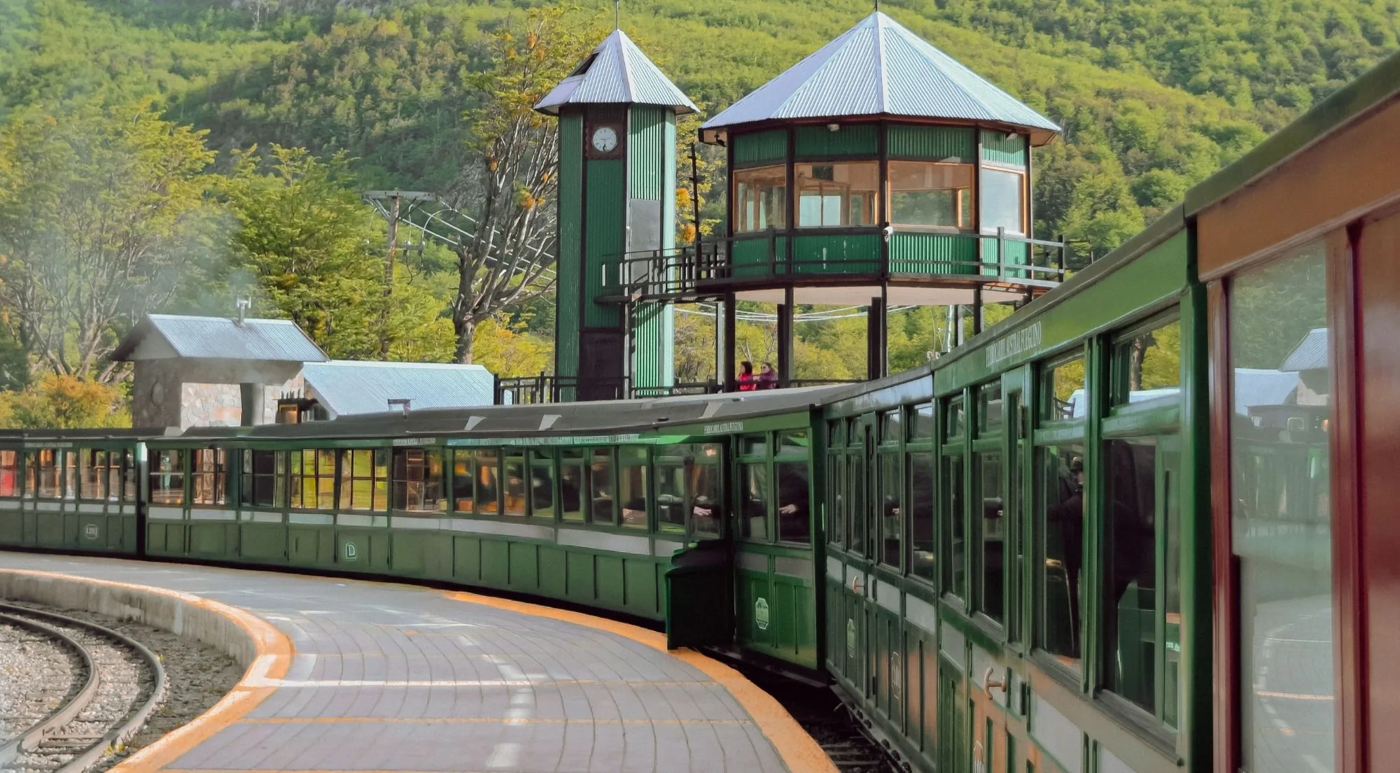 Green carriages of the End of the World Train curving past a wooden station tower